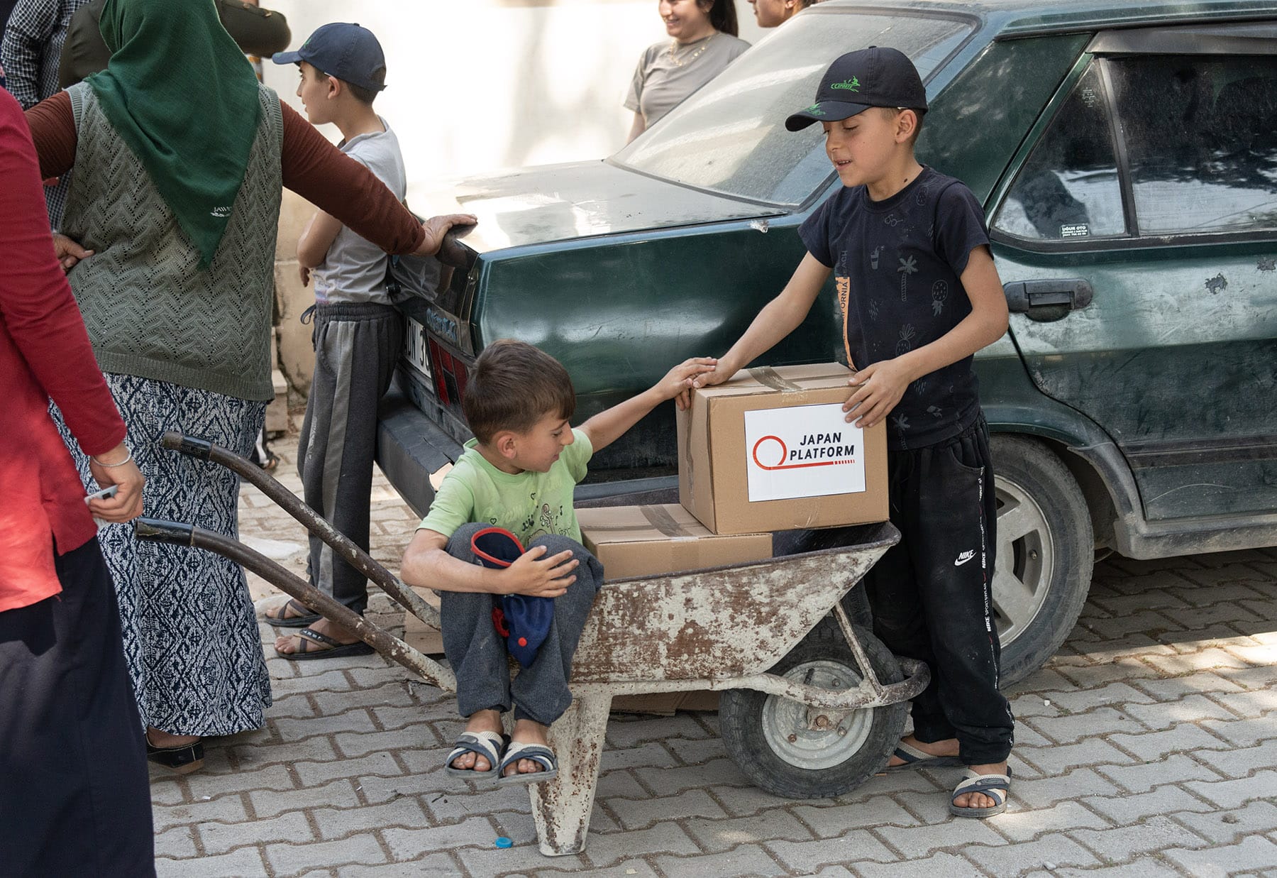 「トルコ南東部地震被災者支援2023」でピースウィンズ・ジャパンが配布した配布した食料品と生活物資の箱を一輪車に積み込む地元の子どもたち。2023年5月12日、トルコ・ハタイ州アンタキヤ市マデンボユ村 ©PeaceWinds